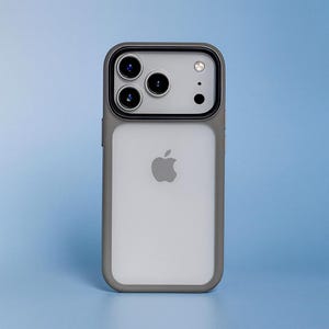 Op de afbeelding: Een grijze en witte telefoonhoes met een doorzichtig cameralensgedeelte. De hoes heeft een grijze rand en een witte achterkant met het Apple-logo. De telefoonhoes staat op een blauwe achtergrond.