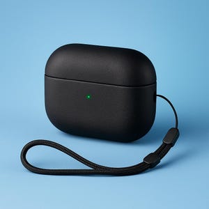Puede incluir: Una funda negra texturizada para auriculares inalámbricos con una correa de muñeca a juego. La funda tiene forma rectangular redondeada y una pequeña luz verde. El fondo es azul claro.