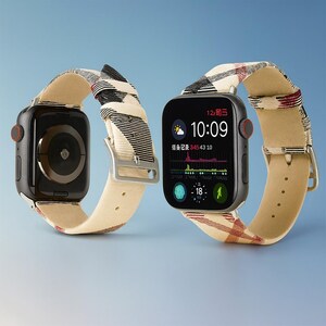 May include: Two black smartwatches with beige and plaid patterned bands. The watch faces display the time, weather, and health data. The bands have silver buckles and red buttons. The background is a gradient of blue.