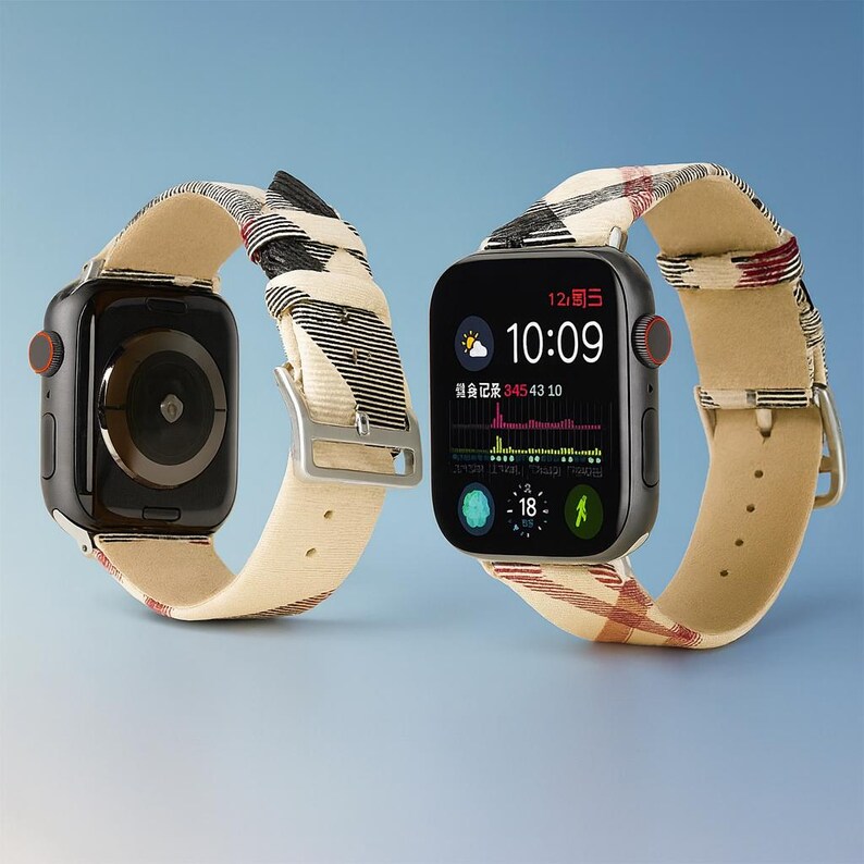 May include: Two black smartwatches with beige and plaid patterned bands. The watch faces display the time, weather, and health data. The bands have silver buckles and red buttons. The background is a gradient of blue.