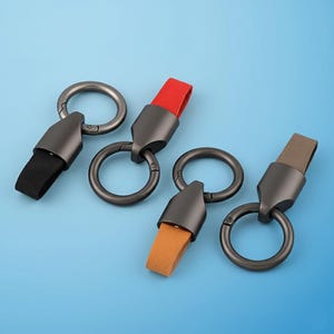 May include: Four keychains with dark gray metal rings and accents. Each keychain has a different colored fabric strap: black, red, orange, and brown. The keychains are displayed on a light blue background.