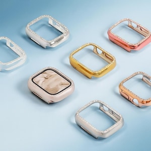 May include: A collection of watch cases in various metallic finishes, including silver, gold, and rose gold. Each case is adorned with sparkling rhinestones around the edges. One case features a marbled face, while others are open-faced.