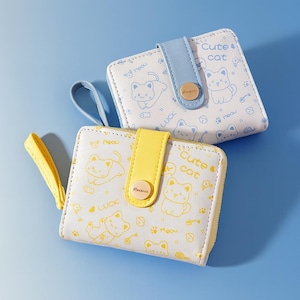 Op de afbeelding: Twee kleine, vierkante portemonnees met kattenillustraties. Eén is wit met gele accenten en de andere is wit met blauwe accenten. Op de portemonnees staan de woorden "Cute cat", "Meow" en "Luck".