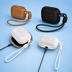May include: Four protective cases for wireless earbuds featuring a woven texture and a matching wrist lanyard. The set includes one brown, one black, and two white cases, with the white cases shown connected to charging cables and a wireless pad.