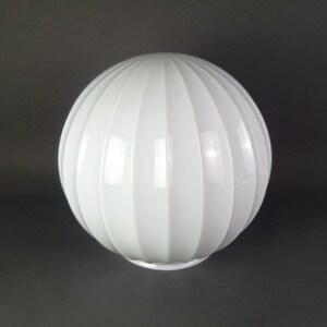 May include: A spherical white glass lamp shade featuring a vertical ribbed texture. The globe has a smooth, glossy finish and a circular opening at the bottom, designed for attachment to a light fixture. The surface reflects light evenly.