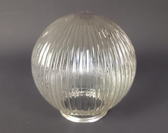 May include: Clear glass globe light fixture with vertical ribbed texture. The round shade has a small opening at the bottom and a slightly pointed top. The glass is transparent, allowing light to pass through.