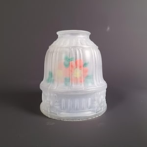 Può includere: Paralume in vetro trasparente smerigliato con un motivo floreale. Il paralume ha una forma arrotondata con creste verticali e una base decorativa. I fiori sono dipinti in tonalità di rosa, giallo e verde.