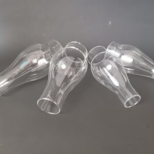 May include: A set of four clear glass lamp shades with a bulbous, teardrop-like shape. Each shade features a narrow opening at the base that widens into a rounded body before tapering slightly toward the top, creating a smooth, transparent silhouette.