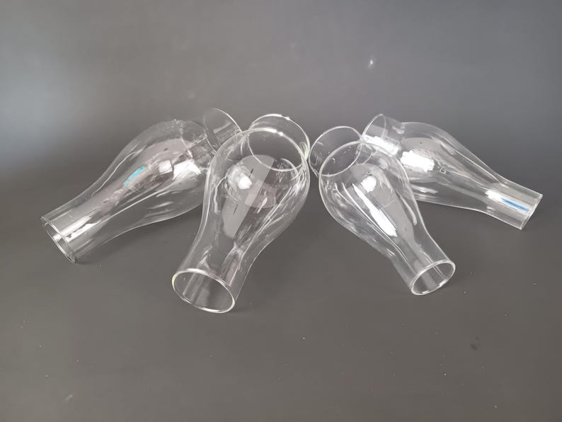 May include: A set of four clear glass lamp shades with a bulbous, teardrop-like shape. Each shade features a narrow opening at the base that widens into a rounded body before tapering slightly toward the top, creating a smooth, transparent silhouette.