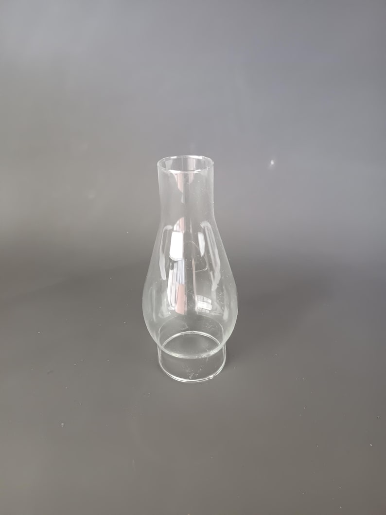 May include: A clear glass oil lamp chimney featuring a bulbous midsection that tapers into a narrow, cylindrical top opening and a wider, circular base designed for secure attachment to a lamp fixture, showcasing a smooth, transparent surface.