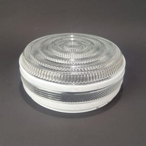 May include: A clear glass light fixture cover with a circular, ridged design on top and a white band around the middle. The cover has a rounded shape and is likely for a ceiling light or similar fixture.