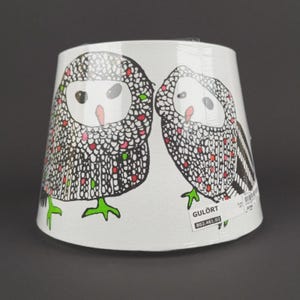 May include: White lampshade featuring two owl illustrations. The owls have black and white patterned bodies with red, green, and pink accents. The owls have white faces, black eyes, and green feet. The lampshade has the text "GULÖRT".