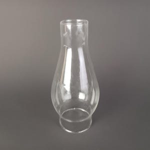 May include: A clear glass lamp chimney with a bulbous midsection that tapers toward a narrow top opening and a wider circular base. The transparent glass features a smooth, reflective surface and a simple, functional silhouette for light fixtures.