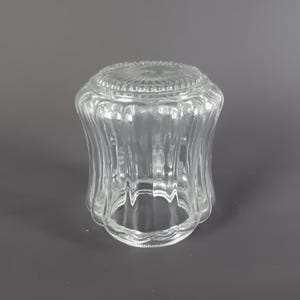 May include: A clear, vintage-style glass lampshade with a ribbed, fluted design. The shade has a rounded top and a flared bottom, suitable for a small lamp or fixture. The glass is transparent, allowing light to pass through.