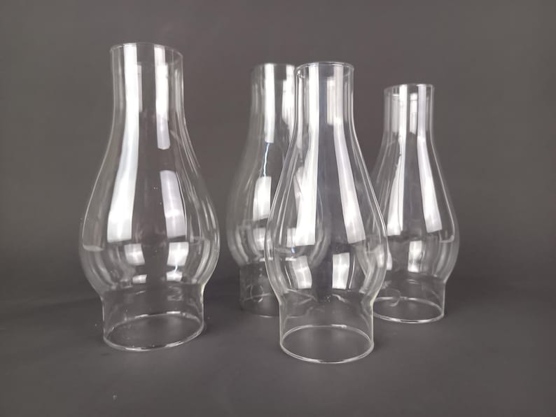 May include: A set of four clear glass lamp chimneys, each featuring a bulbous midsection that tapers toward a narrow top opening and a wider base. The transparent glass shades are arranged in a cluster, showcasing their smooth, curved silhouettes.