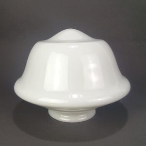 May include: A smooth, glossy white glass light fixture shade with a bell-shaped profile. The shade features a rounded top, a wide flared midsection, and a circular base opening designed for attachment to a lighting fixture or lamp socket.