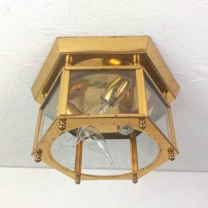 May include: A hexagonal flush mount ceiling light fixture with a polished gold metal frame and clear glass panels. Each glass panel features a delicate etched starburst pattern. The interior contains a single light bulb socket.