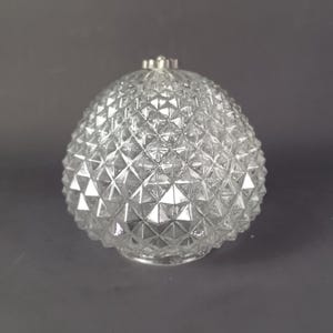 May include: Clear glass decorative object with a diamond pattern. The object has a silver-colored top and base. The glass is transparent, allowing light to pass through. The object is egg-shaped.