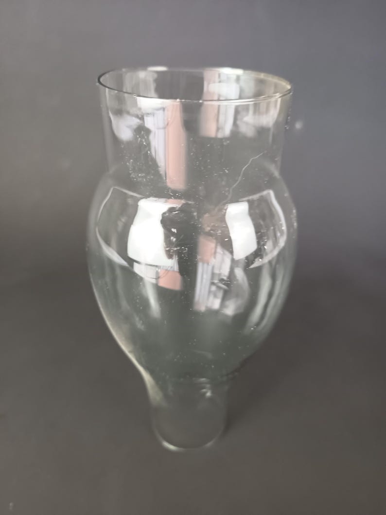 May include: A clear glass vessel featuring a wide, rounded bulbous body that tapers into a narrower cylindrical neck at the top and a smaller circular base at the bottom, showcasing a smooth, transparent surface with subtle light reflections.