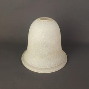 Puede incluir: Una pantalla de lámpara de vidrio en forma de campana con un acabado esmerilado y texturizado. La pantalla presenta una apariencia blanca translúcida con un patrón de superficie sutil e irregular y una abertura circular en la parte superior.