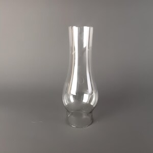 May include: A clear glass lamp chimney with a bulbous base that tapers into a slender, straight neck. The transparent glass features a smooth, reflective surface with a wide opening at the bottom and a slightly narrower opening at the top.