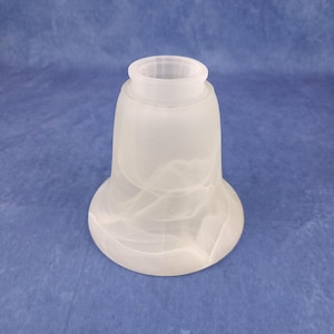 May include: A frosted glass lampshade with a flared, bell-like shape. The white glass has a marbled appearance, with swirling patterns throughout. The lampshade has a cylindrical top and a rounded base. The background is a solid blue.