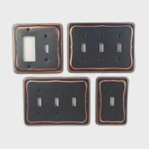 May include: A set of black metal light switch covers with copper-coloured trim. The set includes covers for single, double, triple, and quad switches. The covers have a rustic, textured appearance.