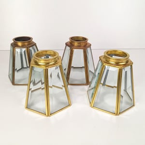 May include: A set of four hexagonal lamp shades featuring clear glass panels framed in metallic gold-toned brass. Each shade has a tapered shape with a circular opening at the top and a wider base, showcasing a clean, geometric construction.