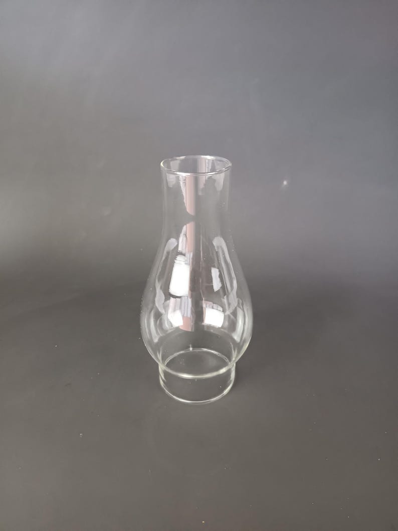 May include: A clear glass lamp chimney with a bulbous midsection and a straight, narrow neck. The glass is transparent and smooth, featuring a wider base that tapers inward before expanding into a rounded body, ending in a straight top opening.