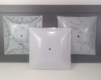 May include: Three square light fixtures. The center fixture is plain white, while the two flanking fixtures have decorative etched designs. The fixtures are mounted on a gray surface, creating a clean and classic aesthetic.