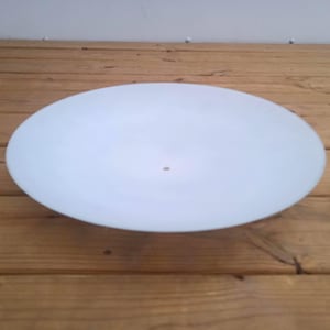 Puede incluir: Un cuenco o pantalla de lámpara circular y poco profunda de vidrio blanco esmerilado con un acabado suave y mate. El objeto presenta una única abertura circular pequeña y centrada, con un aspecto limpio, minimalista y translúcido.