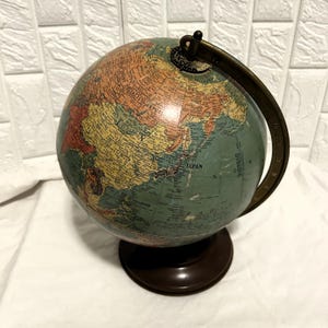 May include: A vintage globe with a brown base and a metal meridian. The globe features a map with various colors, including green, orange, and yellow, and is mounted on a dark brown stand. The globe is a decorative item.