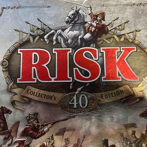 May include: Risk Collector's 40th Anniversary Edition board game box. The box features a red and white logo with a mounted soldier illustration. The box has a silver background with a banner that reads "Collector's Edition".