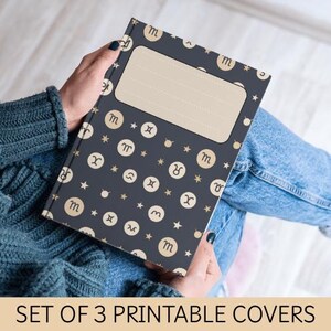 Peut inclure: Une couverture de cahier bleu foncé ornée de symboles du zodiaque et d'étoiles. Elle comporte une zone d'étiquette rectangulaire beige. Le texte "SET OF 3 PRINTABLE COVERS" est en bas de l'image.