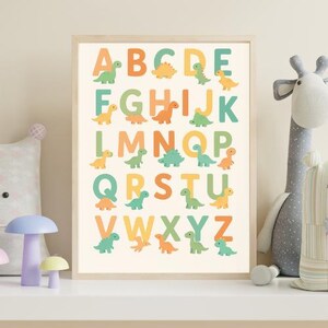 Peut inclure: Une affiche encadrée de l'alphabet avec des lettres colorées et des illustrations de dinosaures. Les lettres sont dans des tons orange, vert et jaune, avec une image de dinosaure à côté de chaque lettre. Le fond est beige clair.