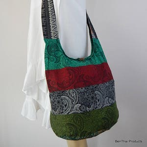 May include: A multi-coloured patchwork hobo bag with a long strap. The bag is made of green, red, black and white fabric with a paisley pattern. The strap is black with white geometric designs.