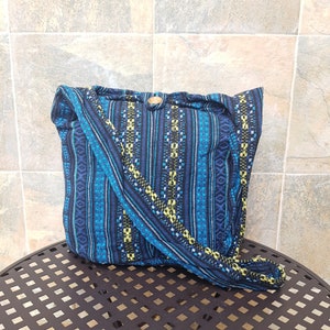 May include: A blue and black striped fabric tote bag with a yellow and green geometric pattern. The bag has a long strap and a wooden button closure.