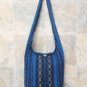 May include: A blue and black striped fabric shoulder bag with a geometric pattern. The bag has a wooden button closure.