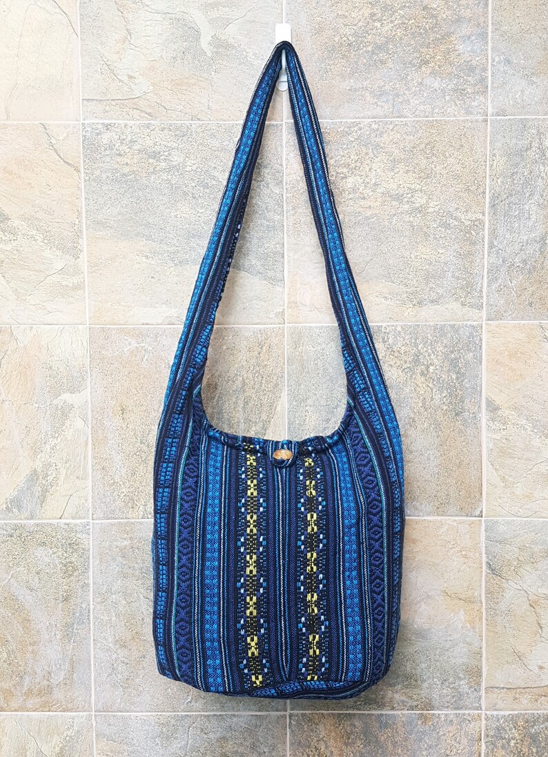 May include: A blue and black striped fabric shoulder bag with a geometric pattern. The bag has a wooden button closure.