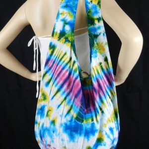 Puede incluir: Una bolsa de mano blanca de tejido tie-dye con detalles azules, verdes, amarillos y rosas. La bolsa tiene una correa larga y está hecha de un tejido suave y ligero.