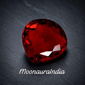 Peut inclure: Une pierre précieuse rouge en forme de cœur à facettes avec une taille brillant et une couleur cramoisie profonde. La pierre présente des facettes géométriques nettes qui reflètent la lumière, créant des reflets vifs. Le texte MoonauraIndia est imprimé en blanc sous la gemme.