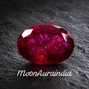 Peut inclure: Une pierre précieuse ovale de couleur magenta profond avec une surface à facettes et des inclusions internes en forme d'aiguilles. La pierre présente une teinte rouge vibrante et translucide avec le texte blanc MoonAuraindia en bas.