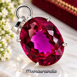 Pode incluir: Um pingente de prata com uma grande pedra preciosa de cor magenta profunda, corte oval e superfícies facetadas. A pedra é fixada por quatro garras de prata e inclui um passador de prata no topo. O texto Moonauraindia está impresso abaixo.