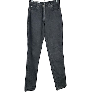 May include: A pair of dark gray denim jeans hanging on a white hanger. The jeans have a classic five-pocket design, a button and zipper closure, and silver rivets. The denim appears to be a medium weight.