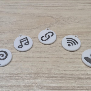 May include: Five white, circular charms with dark gray icons. The icons include a musical note, a chain link, a WiFi symbol, a person, and a spiral. Each charm has a small hole at the top.