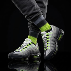 May include: A pair of gray, black, and white sneakers with neon green accents. The sneakers are paired with gray sweatpants and socks with a neon green design. The shoes have a visible air bubble in the heel.
