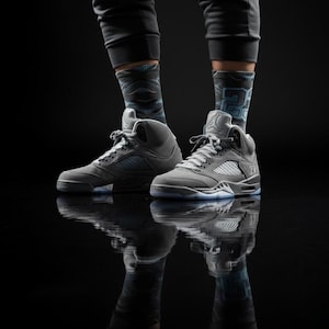May include: A pair of grey high-top trainers with white laces and a translucent sole. The trainers are paired with grey and blue patterned socks and dark grey trousers. The shoes are reflected in the glossy black surface.