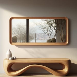 Può includere: Una moderna consolle in legno con un design unico e fluido. Sopra, uno specchio rettangolare con angoli arrotondati riflette una scena esterna. Un vaso in ceramica bianca e grigia e piccole ciotole sono sul tavolo.