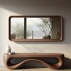 May include: A modern, minimalist interior scene featuring a large, rectangular wooden mirror with rounded corners. Below, a matching wooden console table with a unique, flowing design. Decorative white and gray ceramic pieces sit on the table.