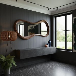 Op de afbeelding: Een modern interieur met een grote, uniek gevormde houten spiegel. Een donkergrijze zwevende kast herbergt decoratieve vazen. Een geweven lamp en een potplant voegen warmte toe aan de ruimte. De muren zijn donkergrijs.